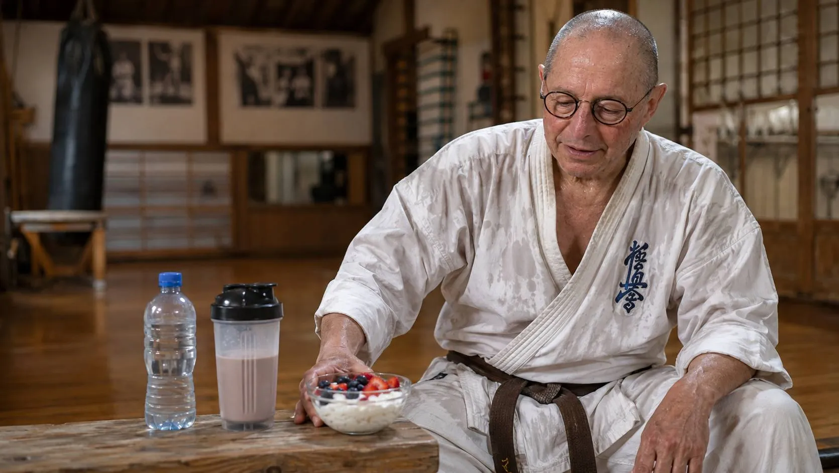 Karateka met bezweet karatepak herstelt na training met water, kwark en eiwitshake in de dojo.